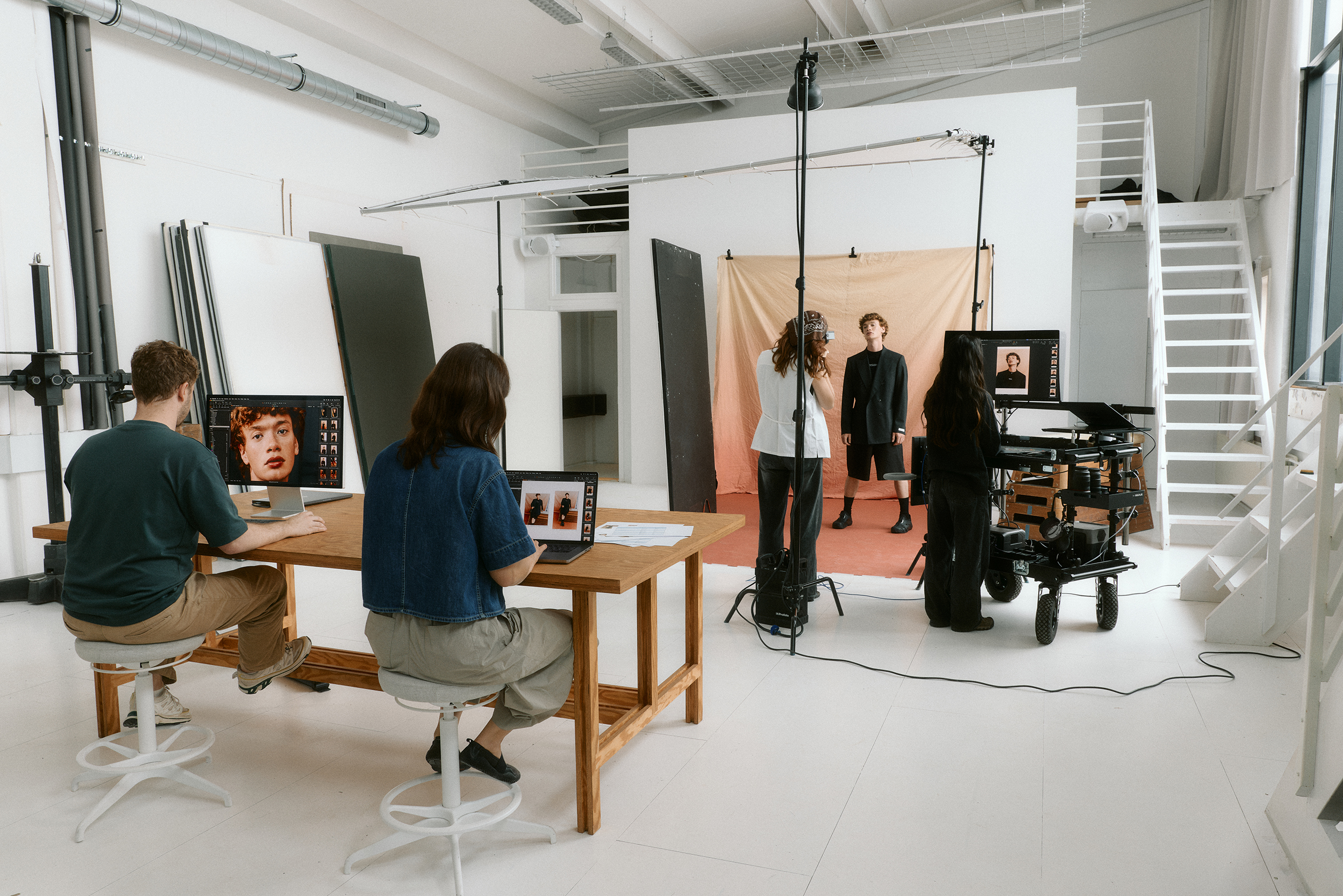 Photo studio with a model posing in front of a backdrop while a photographer and assistants manage cameras and review images on computers