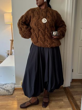 Nnenna in a brown sweater and brown flats.