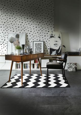 home office with zany monochrome rug and polka dot walls, with a wooden desk and leather chair, and lots of artwork