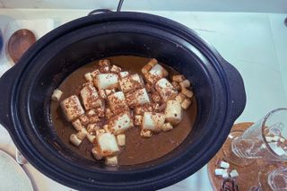 hot chocolate in a slow cooker topped with marshmallows and chocolate flake pieces