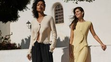 Two female models, one wearing a cream cardigan and black trousers from Whistles, and the other wearing a butter yellow dress from Whistles.