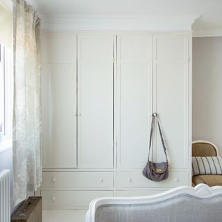 A bedroom with a built-in cream wardrobe and light taupe walls with a contrasting white ceiling