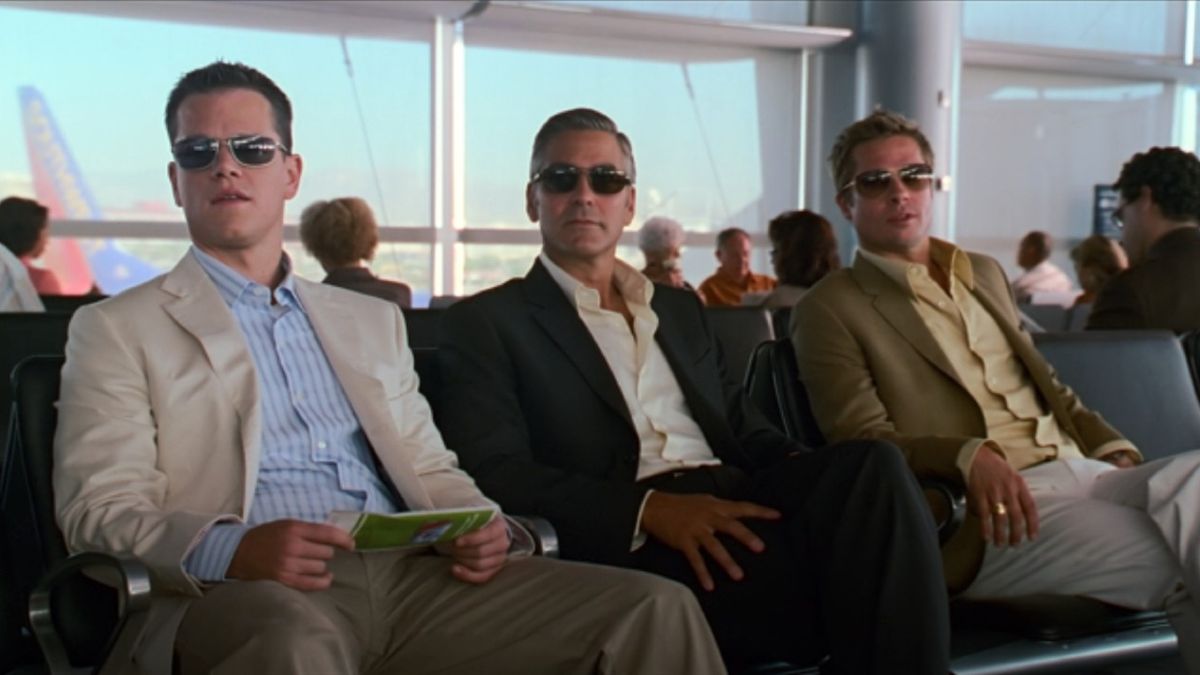 From left to right: Matt Damon, George Clooney, and Brad Pitt sitting in an airport. They&#039;re all wearing sunglasses and looking to the left.