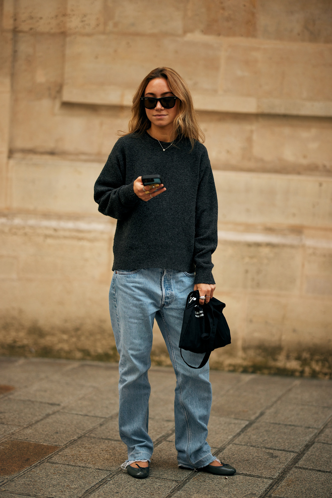 woman wearing black pullover over baggy blue jeans and holding a handbag