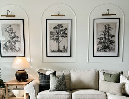 A neutrally decorated living room with three arched wall panels framing picture frames and brass picture lights 