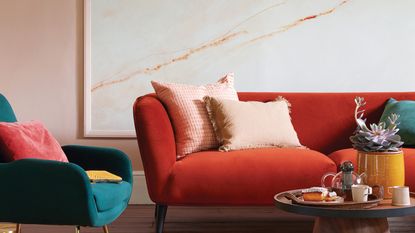 Dusky pink living room with oversized piece of wall art with marbled finish and a rust colour sofa lined with pink cushions