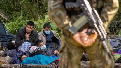 A Polish border guard stands watch over a group of migrants