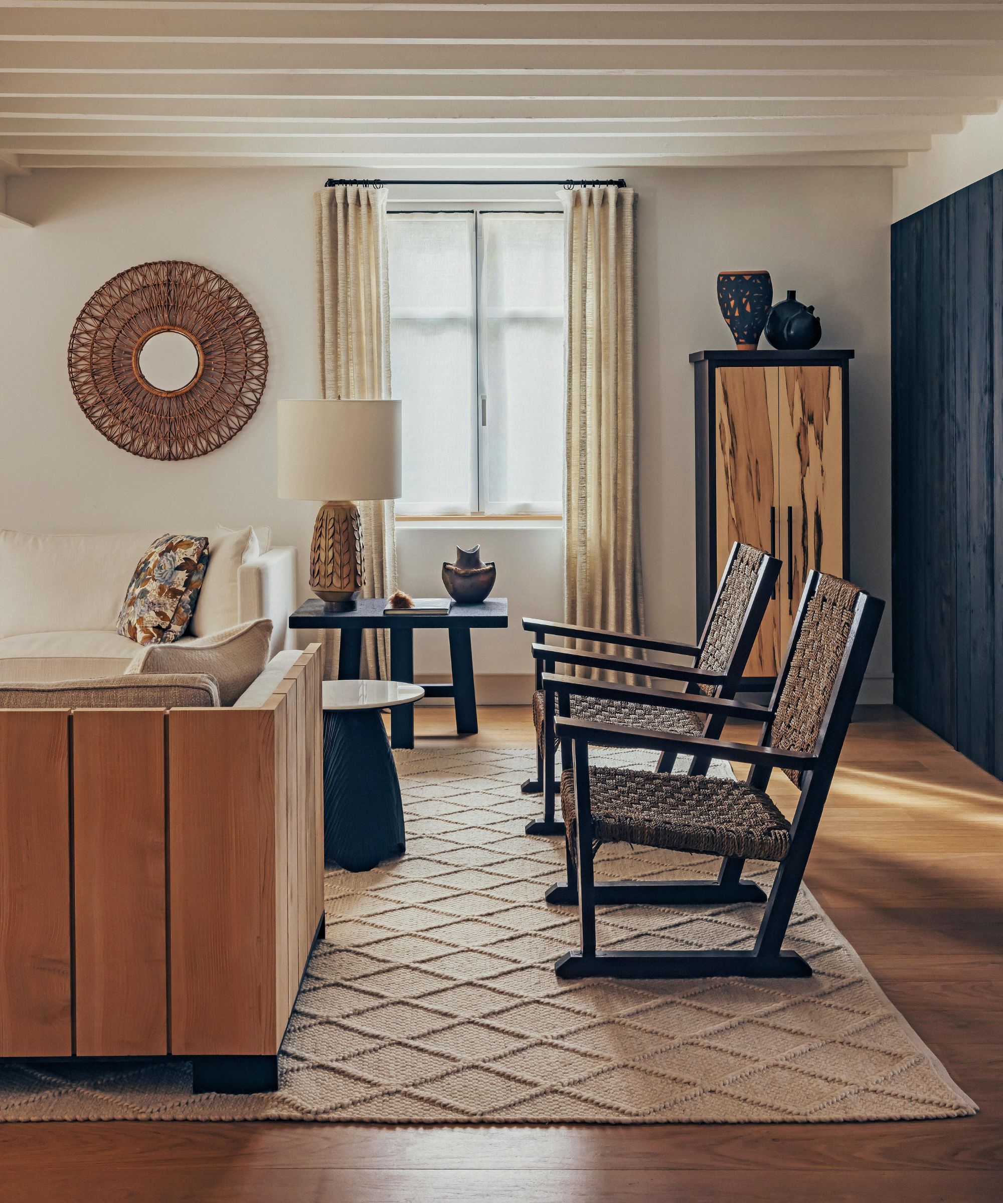 a rustic living room in a home in france with ceiling beams wooden floor, rattan armchairs and accessories