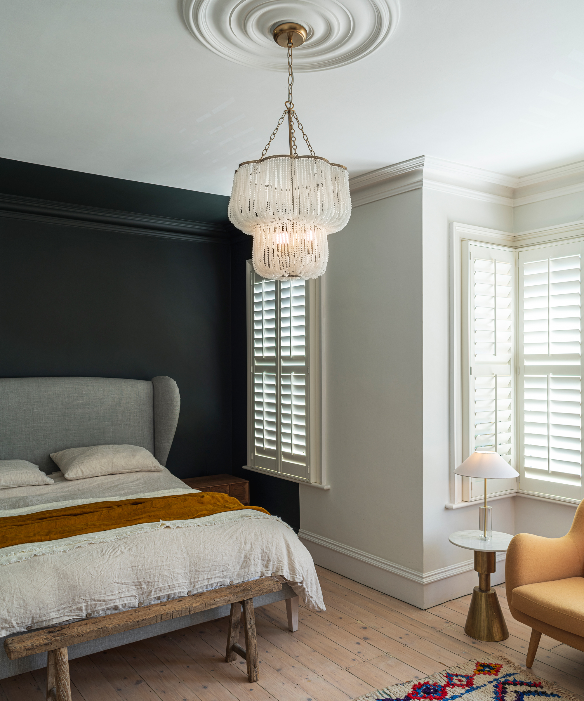 Statement pendant light in sophisticated bedroom with mono contrast walls, grey upholstered winged headboard, and mustard accent chair and throw.