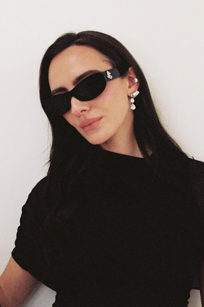 a woman wearing a black top, black sunglasses, and pearl drop earrings