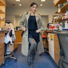 A photo of Vivian Li in a science lab wearing a black dress, argyle tights, a trench coat, and black ballet flats