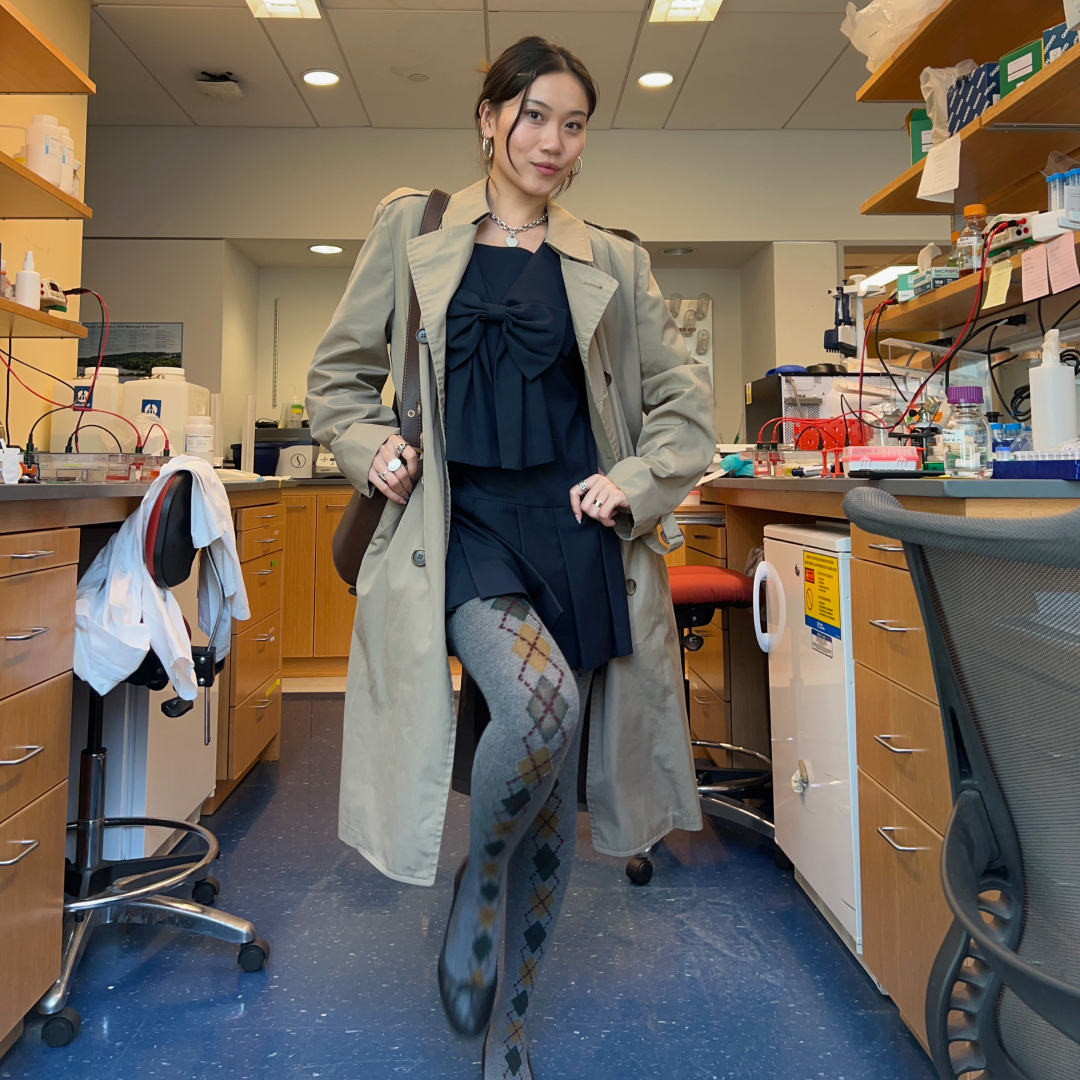 A photo of Vivian Li in a science lab wearing a black dress, argyle tights, a trench coat, and black ballet flats