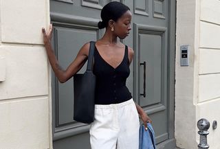 French influencer Sylvie Mus wears Mango black tank top and Mango white trousers, leaning against a door in Paris.