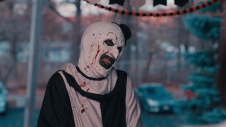 A bloody clown smiles creepily at someone off-screen in Terrifier 2