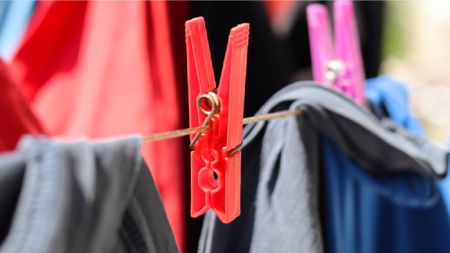 A red clothespin clamping clothes onto a line, clearly displaying its inner circular cutouts