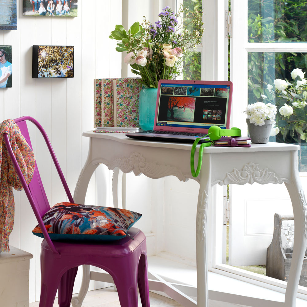 room with white wall with pictures and white desk with pink chair and cushion