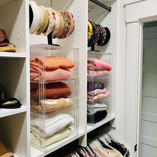 Organized closet with folded jumpers in stacked, clear boxes, and hairbands on hanger