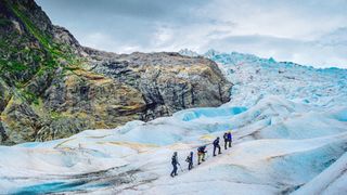 A group crosses a glacier while roped together