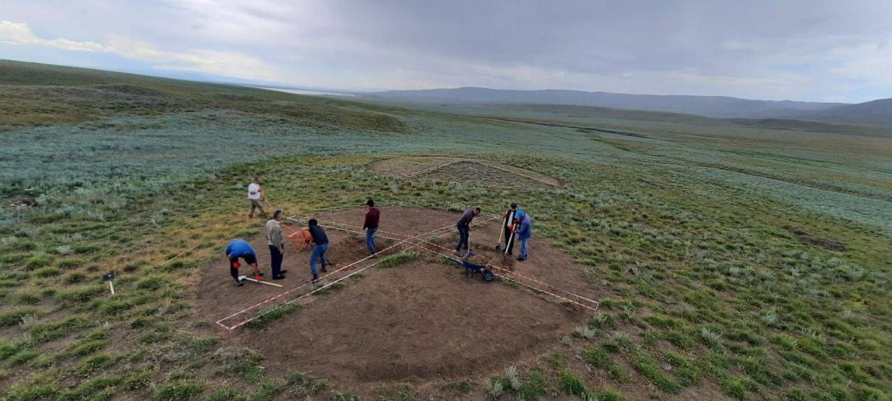 a group of people stand on a dirt mound in a grassy field
