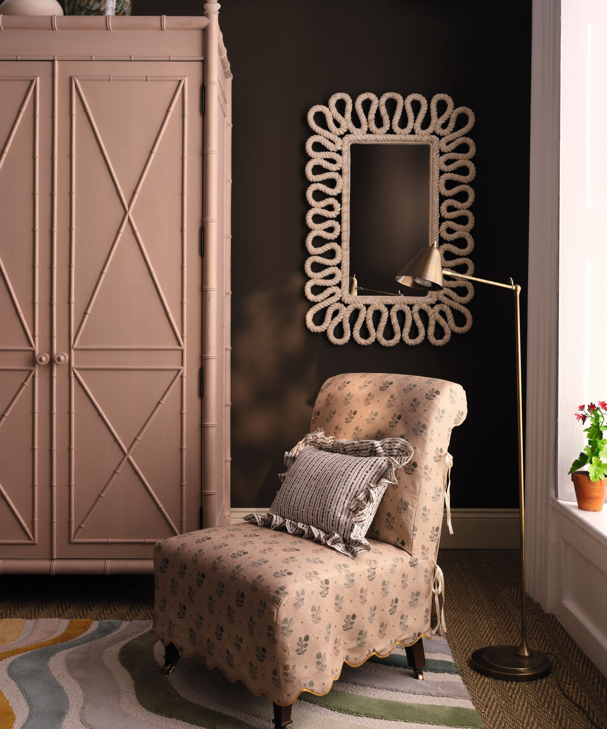 a dark brown room with a large pink-painted cabinet, a floral accent chair with a pillow, a floor lamp, and a mirror on the wall