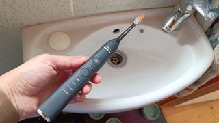 Philips Sonicare DiamondClean Smart toothbrush in testing, with Caramel Quin holding brush above sink