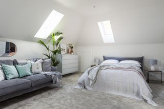 an all-white loft conversion with grey carpet, a grey sofa and grey bed in the middle, and a plant next to white chest of drawers – loft conversion used to add value to a house in this scheme by interior designers Cream & Black