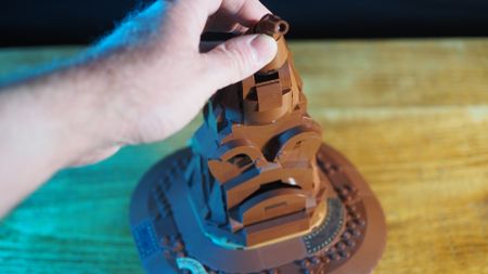 A hand presses the top of the Lego Talking Sorting Hat on a wooden table