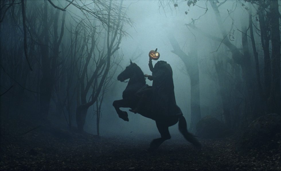 A headless horseman holds up a pumpkin for a head as his horse rears