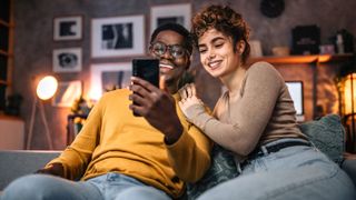 Young couple sitting on sofa, surfing the net using smart phone