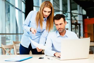 A man and a woman compare their work in an office.