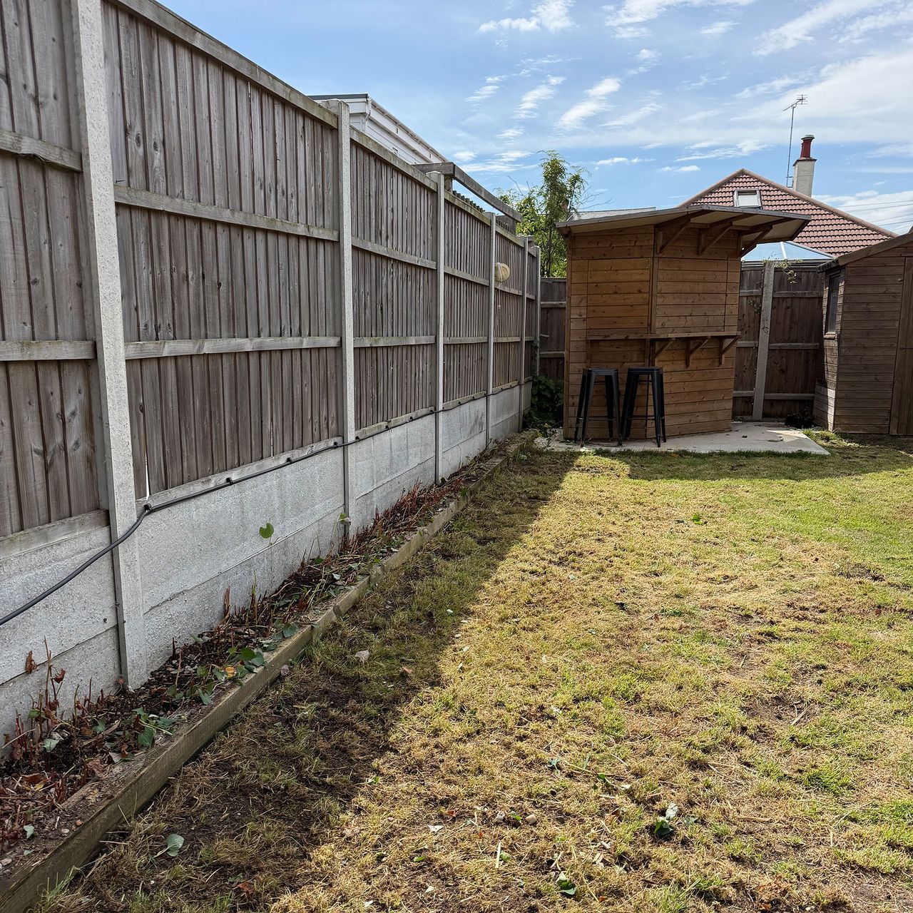 Lawn in garden surrounded by wooden fence with wooden garden bar at end