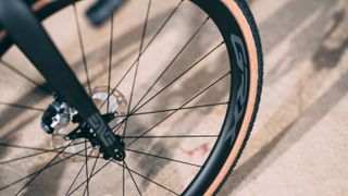 A close up of a wheel with a tanwall gravel tyre mounted on a dusty track