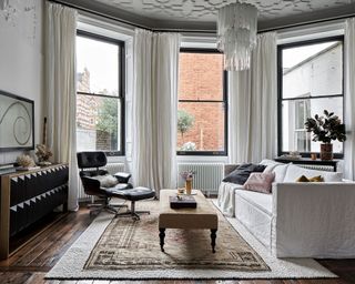 A neutral living room with monochromatic accents, glass chandelier, white sofa and black leather recliner.