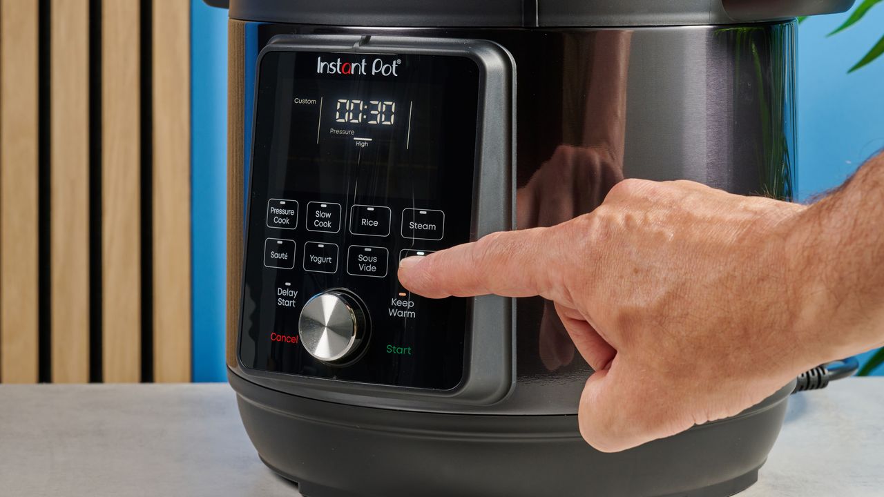 a black instant pot with a dial and touchpad is photographed against a blue background