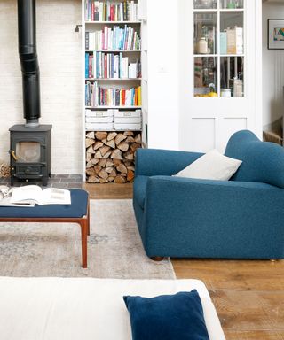 A minimalist living room with a woodburner, a bookshelf and a blue armchair