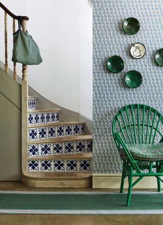 Blue patterned wallpaper ideas in a hallway with wooden staircase and green painted wicker chair.