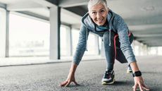 A fit female runner with white hair crouches in the ready position as if poised to start a race.