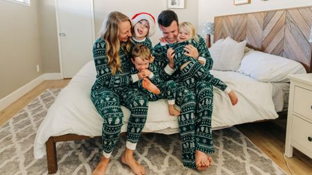 A young family sit on a bed wearing matching green pajamas with a festive pattern. 