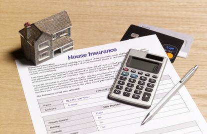 Home insurance application laying on table with calculator, pen and miniature house.