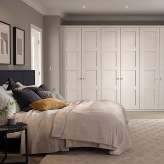 grey bedroom with dressed bed and floor to ceiling white wardrobes
