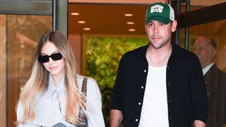 Sydney Sweeney in a button down and black sunglasses and Scooter Braun in a black open button down, a white tee and a baseball cap spending time together.