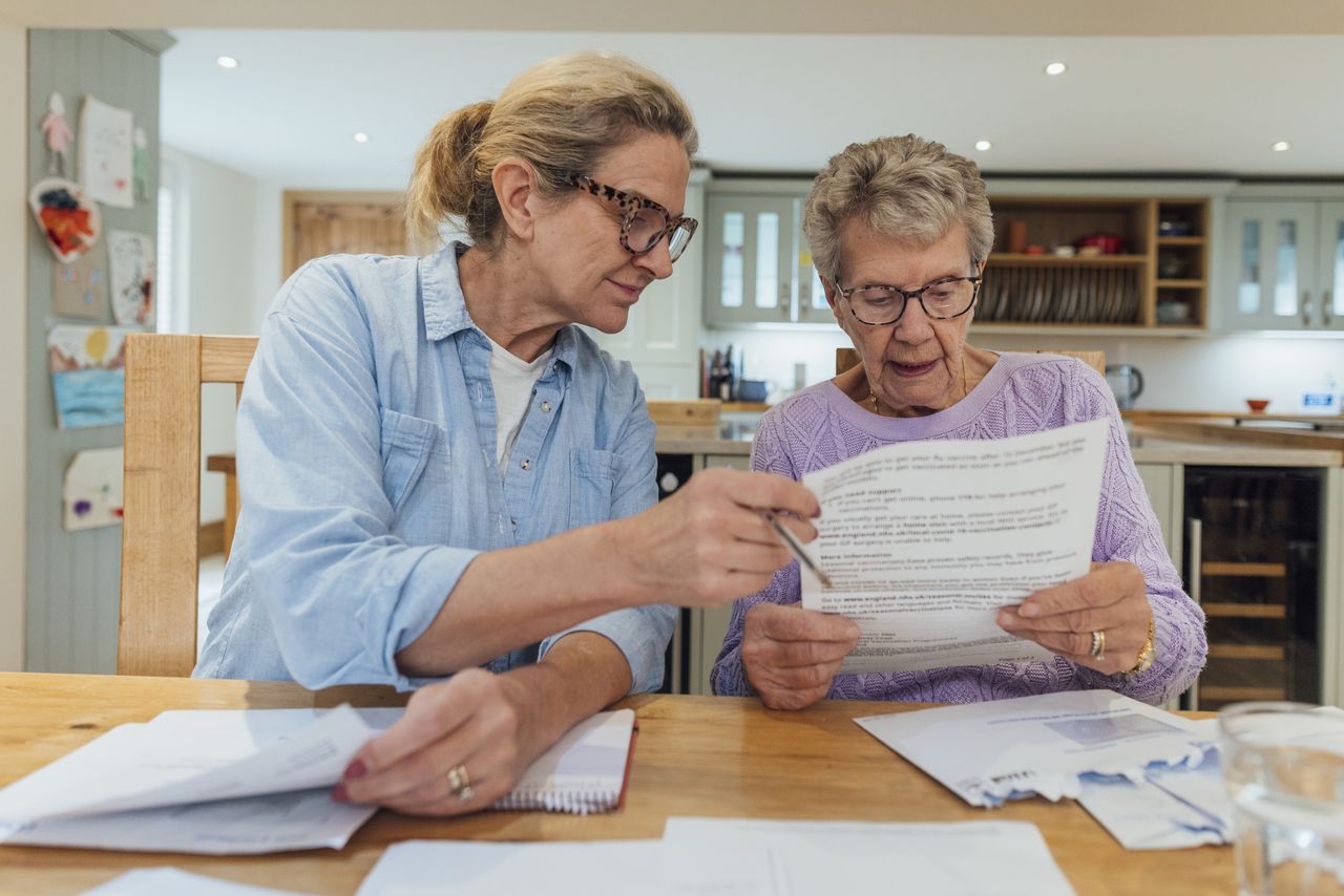 An older woman and her mature daughter at home in Seghill, Northumberland. The senior woman is staying with her daughter for support and care as she has dementia. They are sat at the dining room table where they&#039;re looking through financial bills, looking concerned.