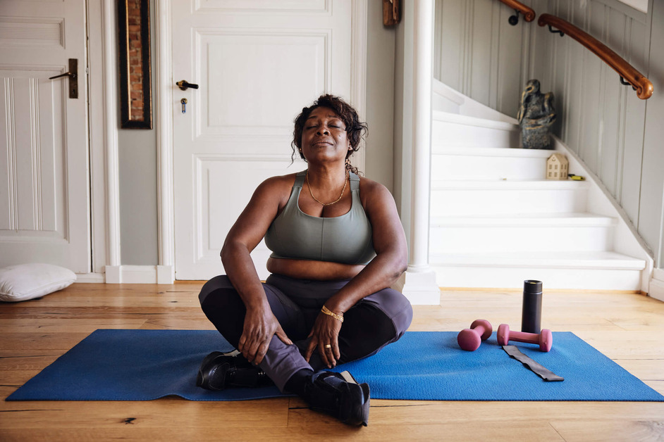 A woman is sitting on a yoga matt during a home workout.