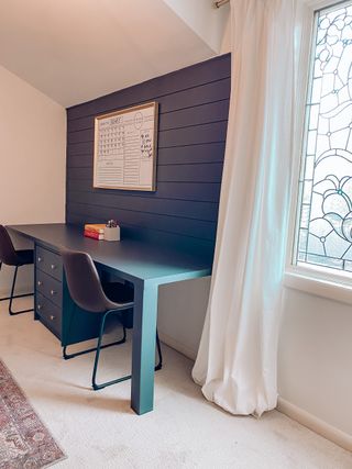 Blue built-in desk with wooden seats, light carpet and white drapes