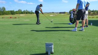 Tiger Woods hits golf balls on the driving range with a launch monitor and caddie behind him