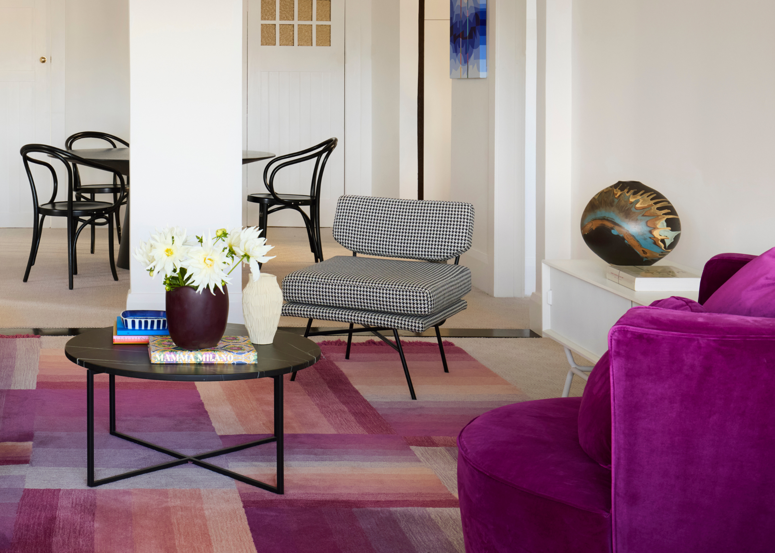 A white living room with a black and white checked accent chair, patterned purple rug, and a purple swivel chair