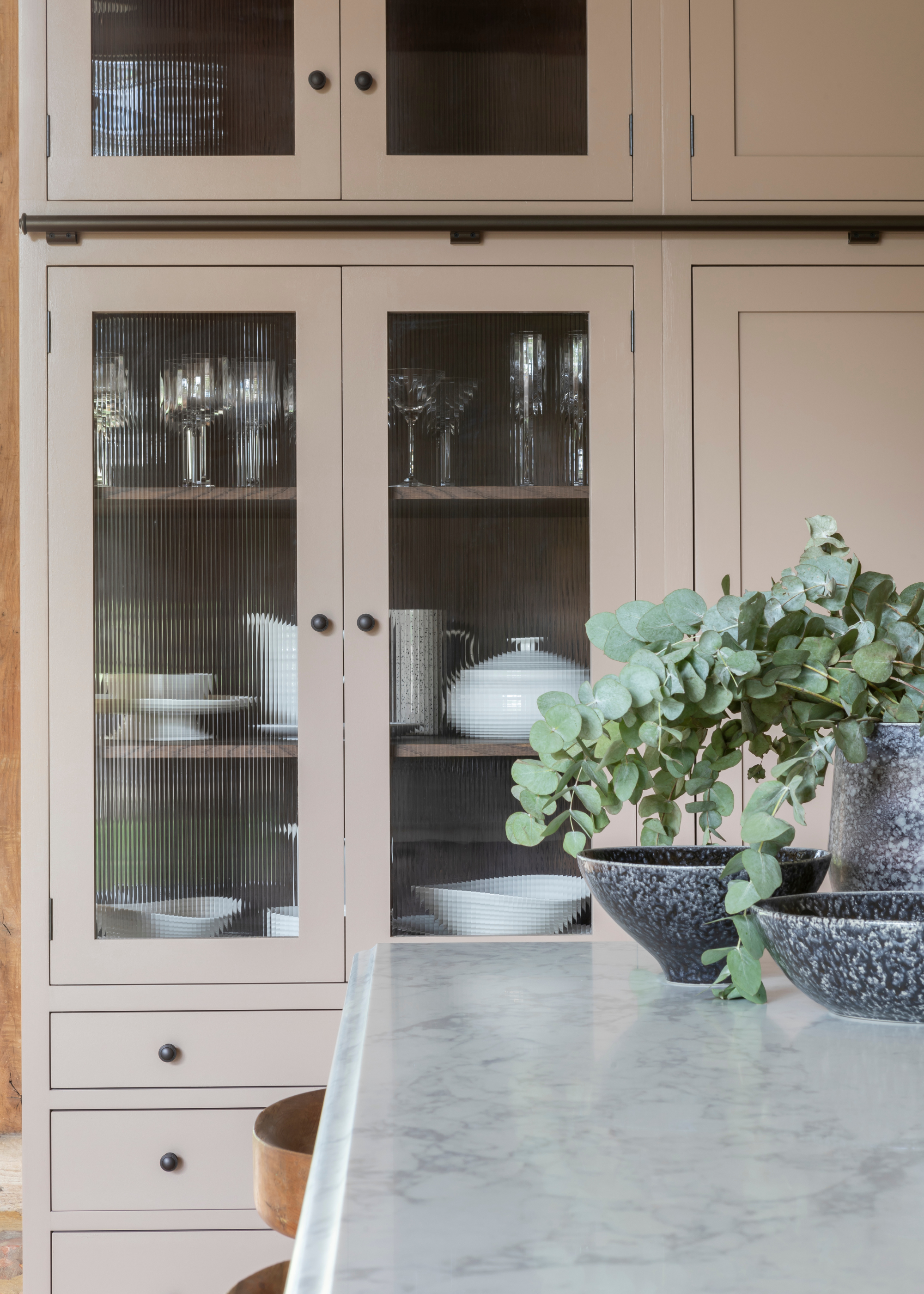 a beige shaker style kitchen with marble tops and fluted glass