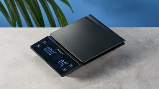 the KitchenTour black coffee scale with a digital LED screen and 0.1g weight accuracy is photographed against a blue background