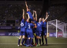 A joyful group of women football/soccer players raise their arms in celebration after a game-winning goal 