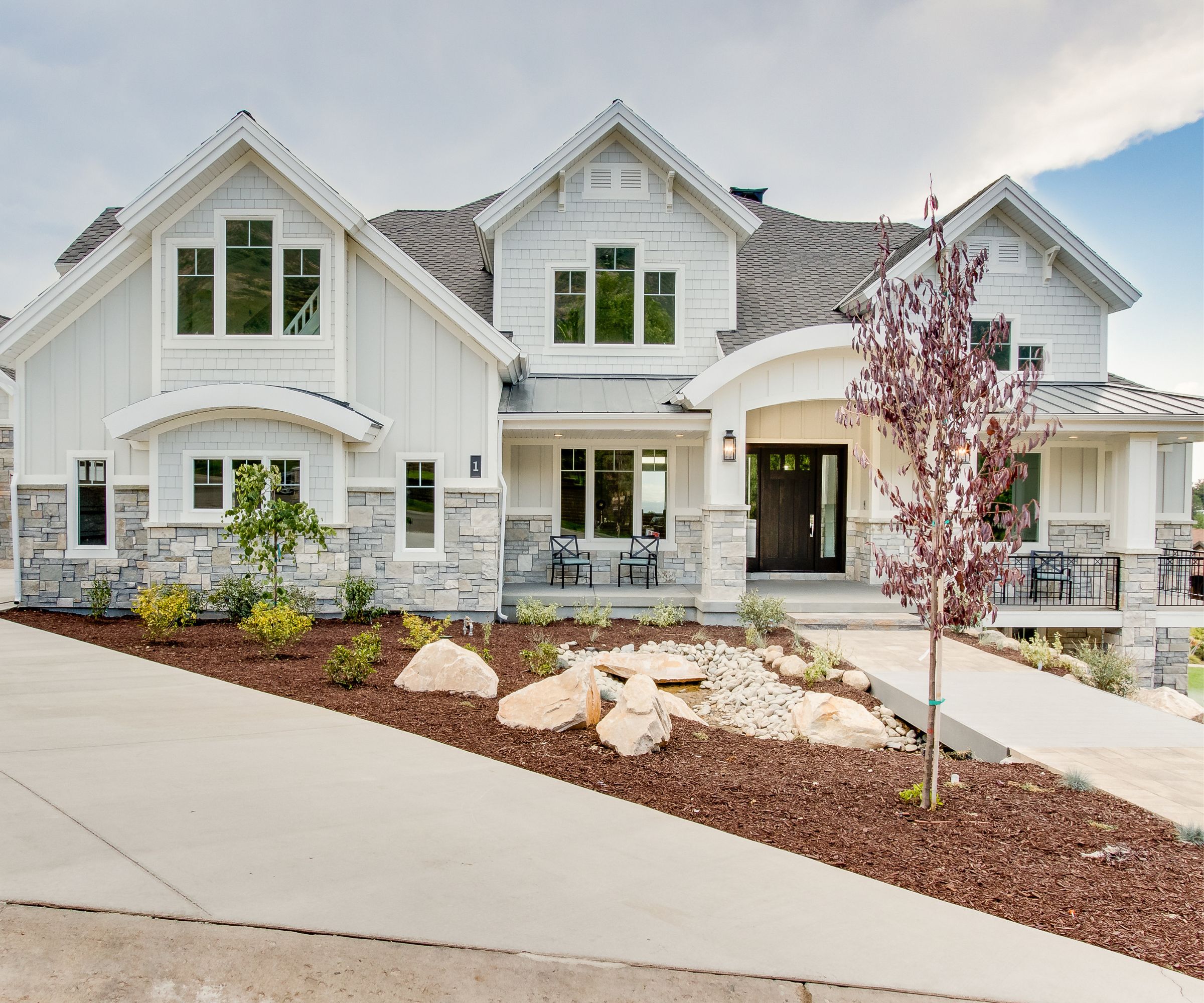 American home with a large front porch, shop lap and slate exterior, painted in Gray Owl by Benjamin Moore, a concrete path and sparse shrubbery.